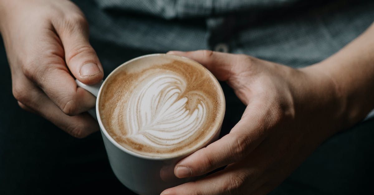 A person is holding a cup of cappuccino with a heart drawn on it.