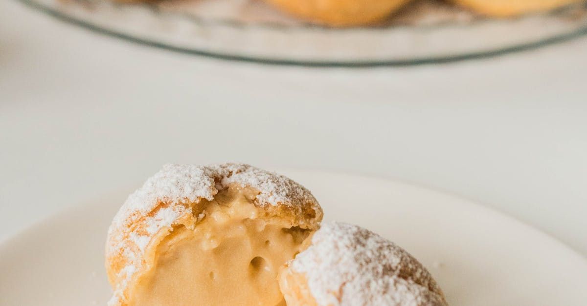 Cream puff halved, filled with cream, dusted with powdered sugar, on a white plate.