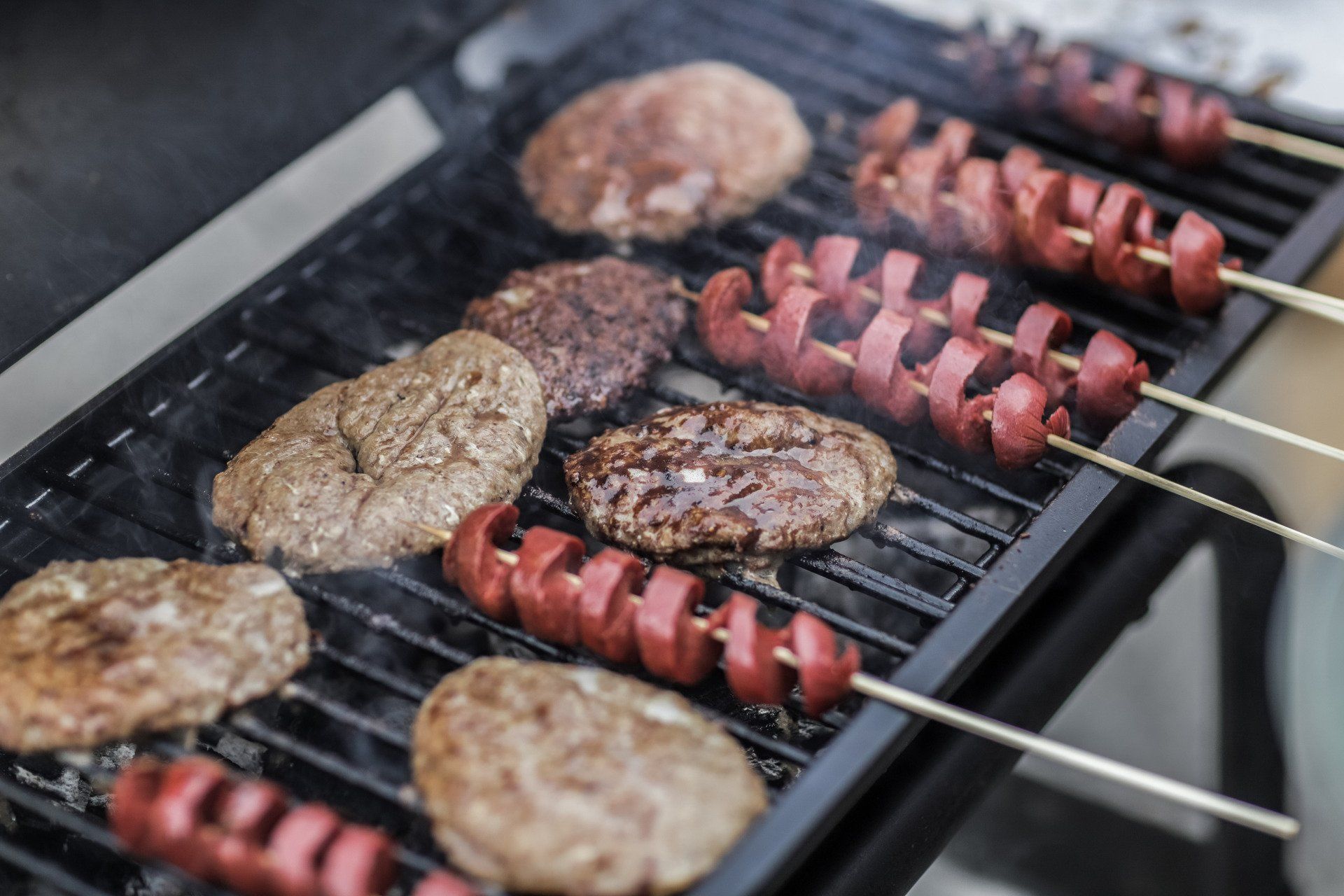 Hamburgers and hot dogs are cooking on a grill