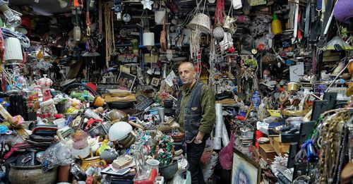 A man is standing in a room filled with lots of items