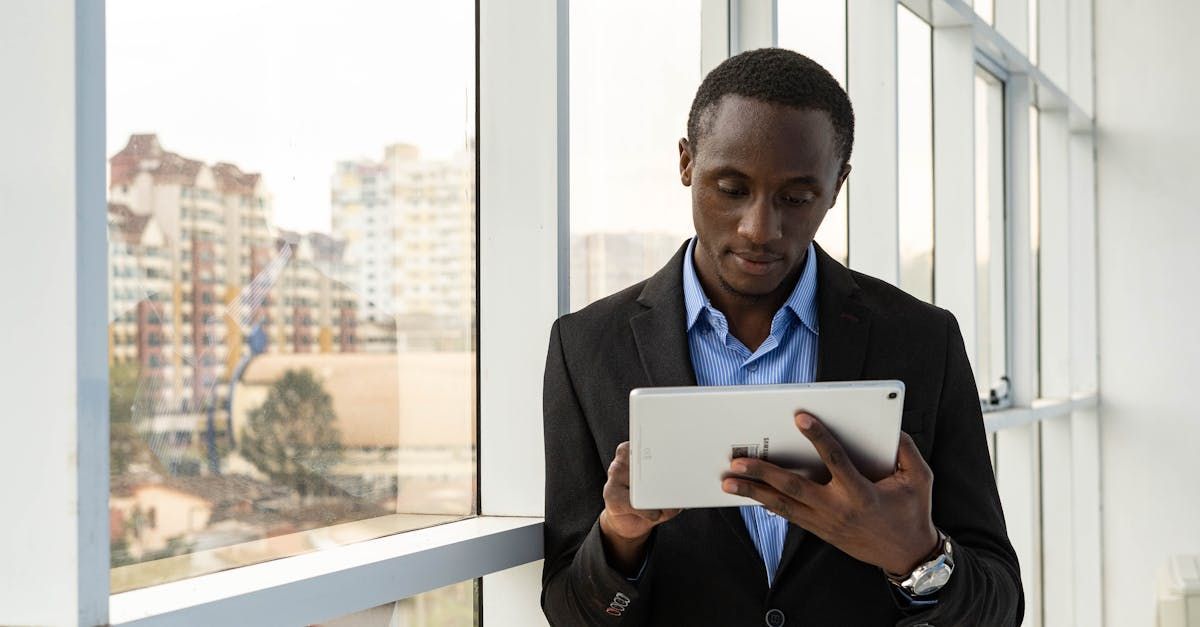 A man in a suit is using a tablet computer in front of a window.