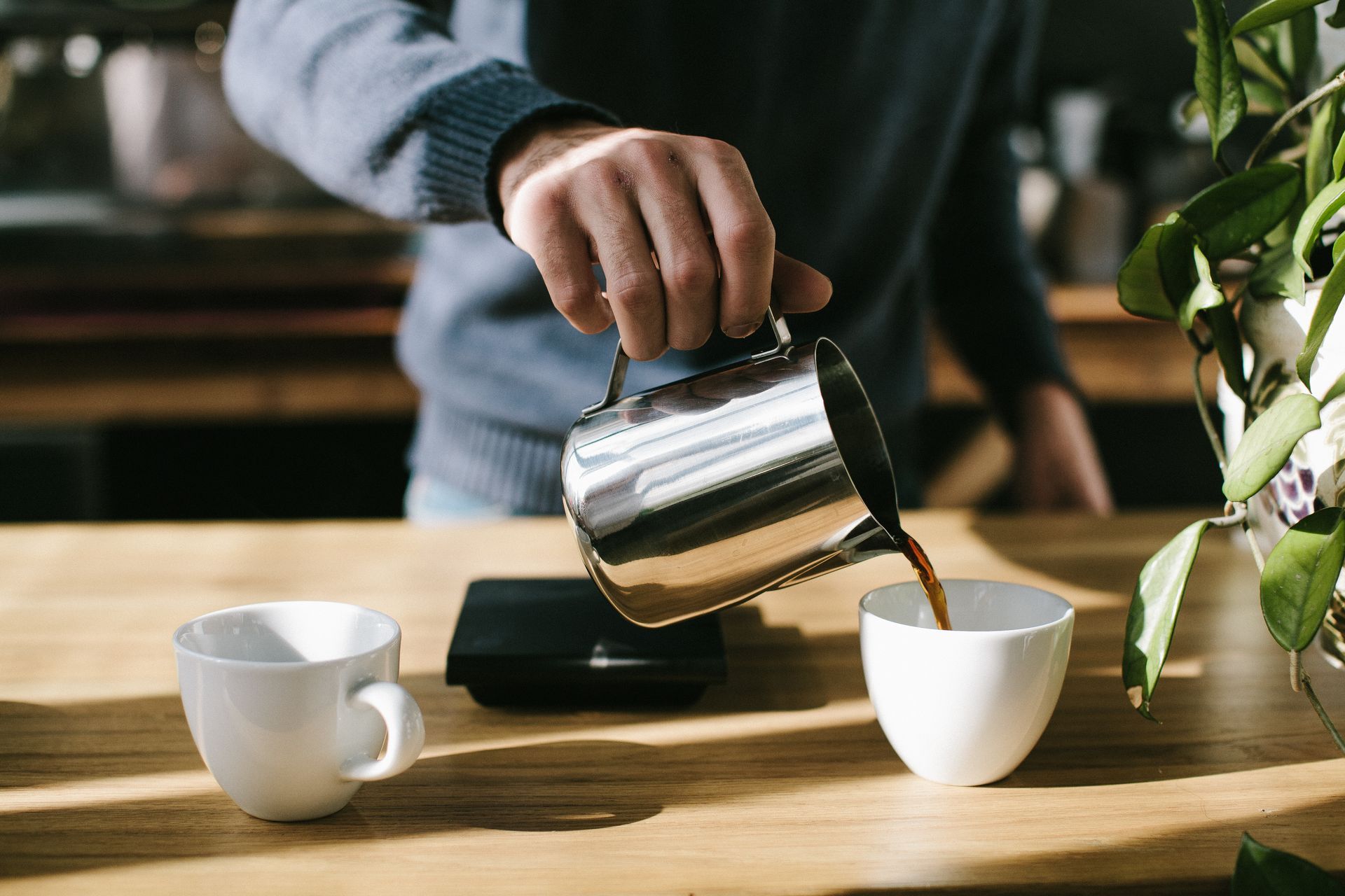 A person is pouring coffee into two cups on a wooden table.
