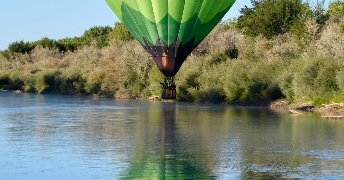 a green hot air balloon is flying over a river