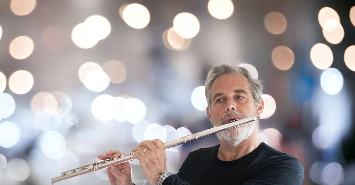 A man with a beard is playing a flute in front of a blurry background.