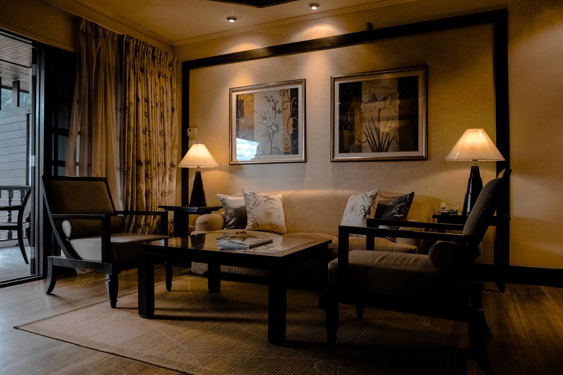 Cozy living room with beige sofa, dark wood furniture, two framed pictures, and soft lighting.