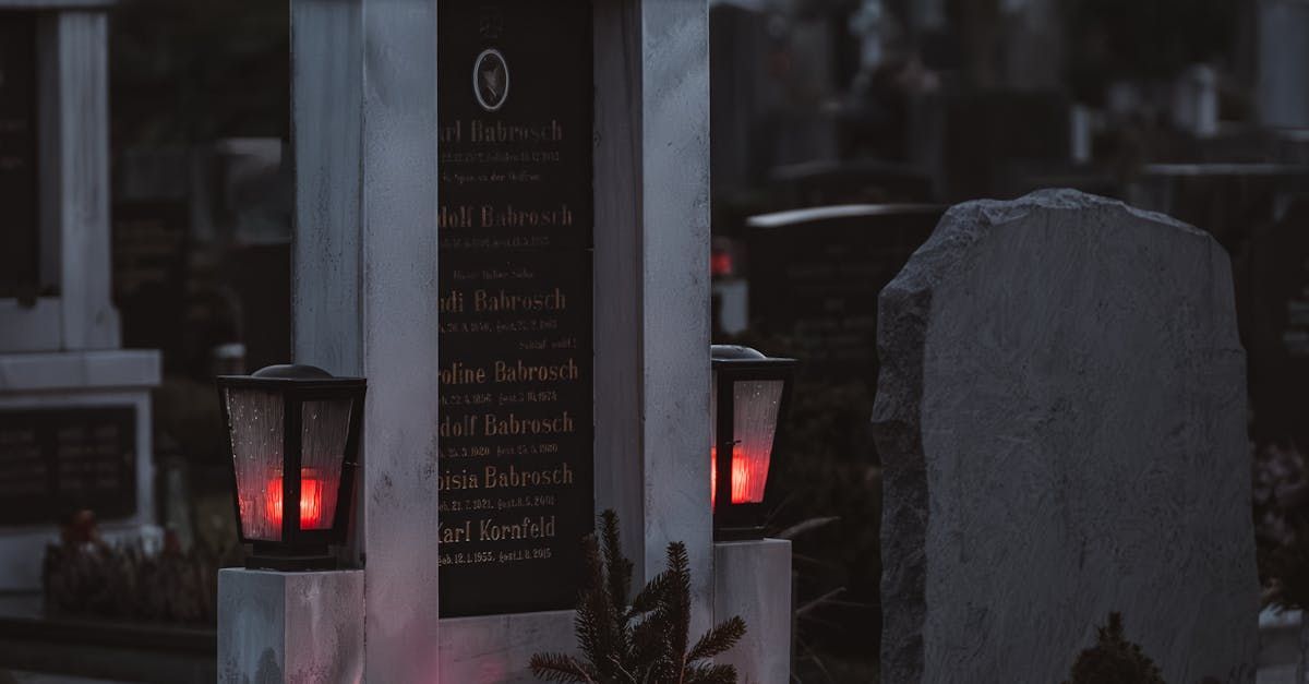 Een donkere, schemerige begraafplaats met rode herdenkingskaarsen die branden naast een hoog, van een steen voorzien monument.