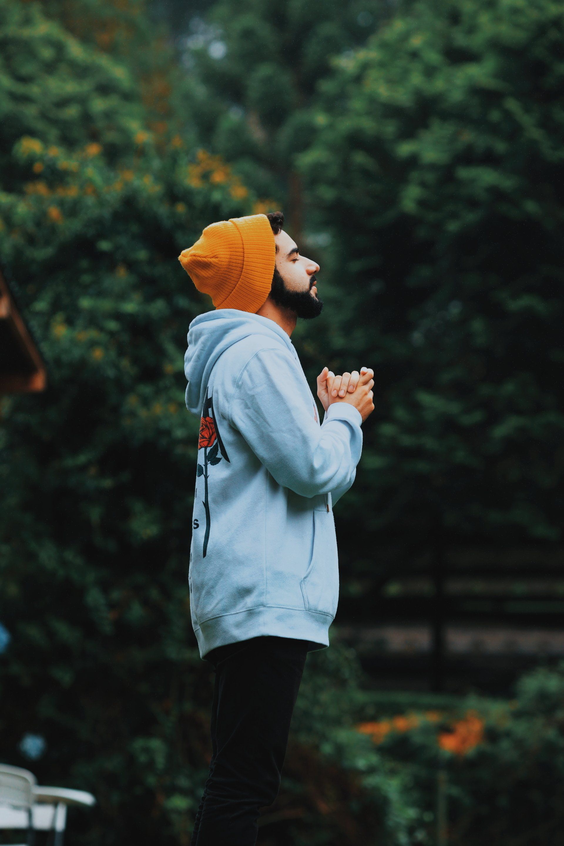 a man wearing a hoodie and a yellow hat is praying in the rain .