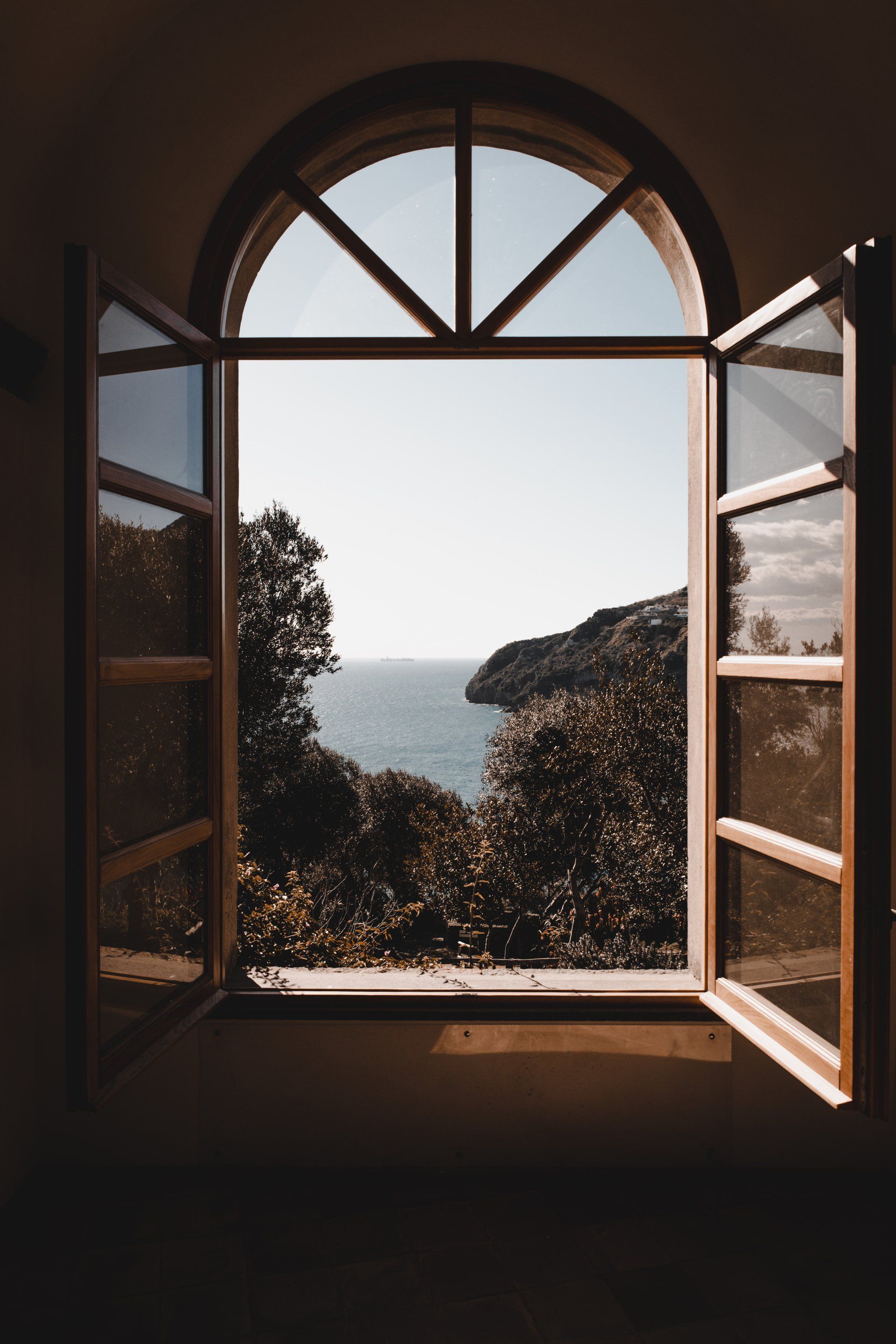 An open window with a view of the ocean and trees
