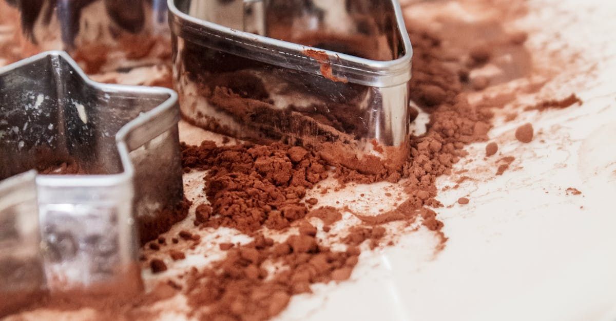 Star and diamond-shaped cookie cutters partially buried in brown cocoa powder on a white surface.