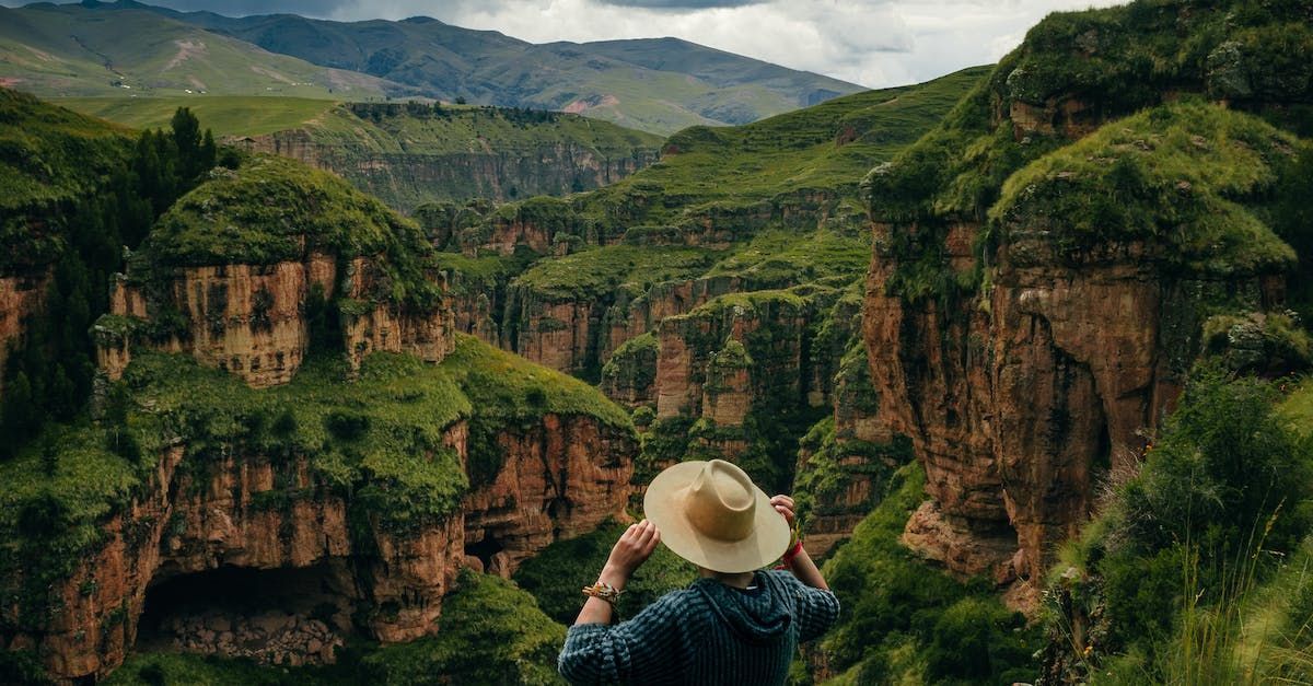 a man in a hat is standing on top of a mountain looking at the mountains .