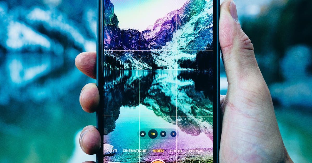 A person is holding a cell phone in their hand and taking a picture of a lake.