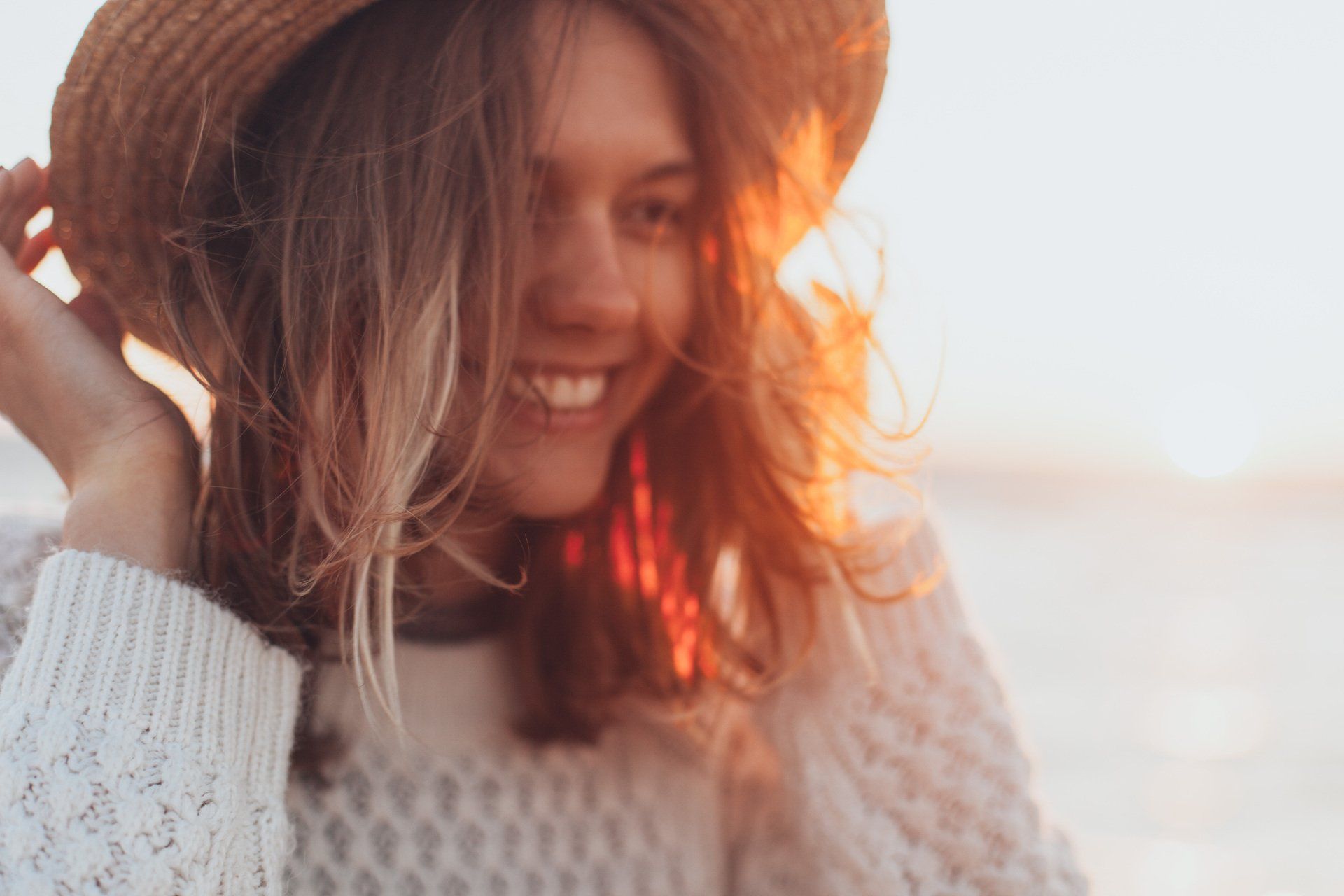 A woman wearing a straw hat and a white sweater is smiling.