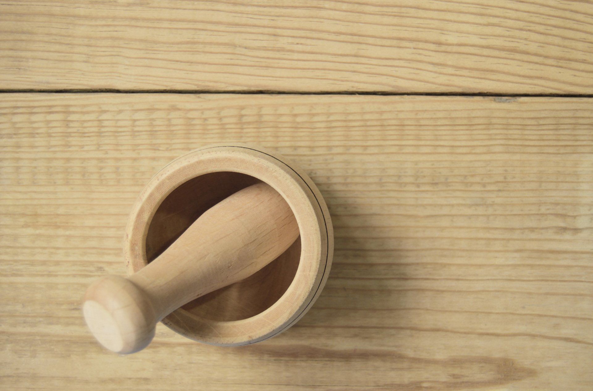 Mortar and pestle made of light wood on a wooden surface.