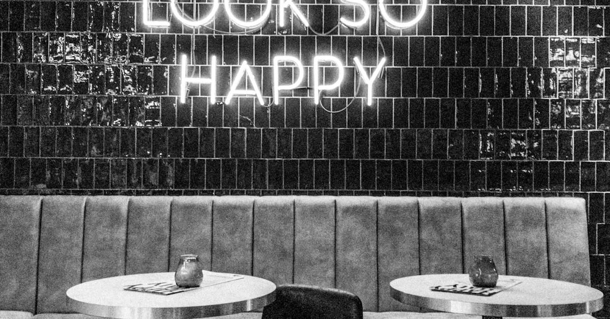 A black and white photo of a restaurant with tables and a neon sign that says happy.