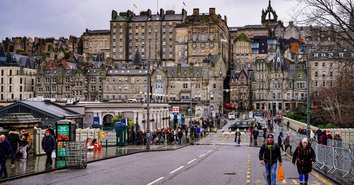 A street scene in Edinburgh featuring historic stone buildings, city traffic, and pedestrians on a cloudy day.