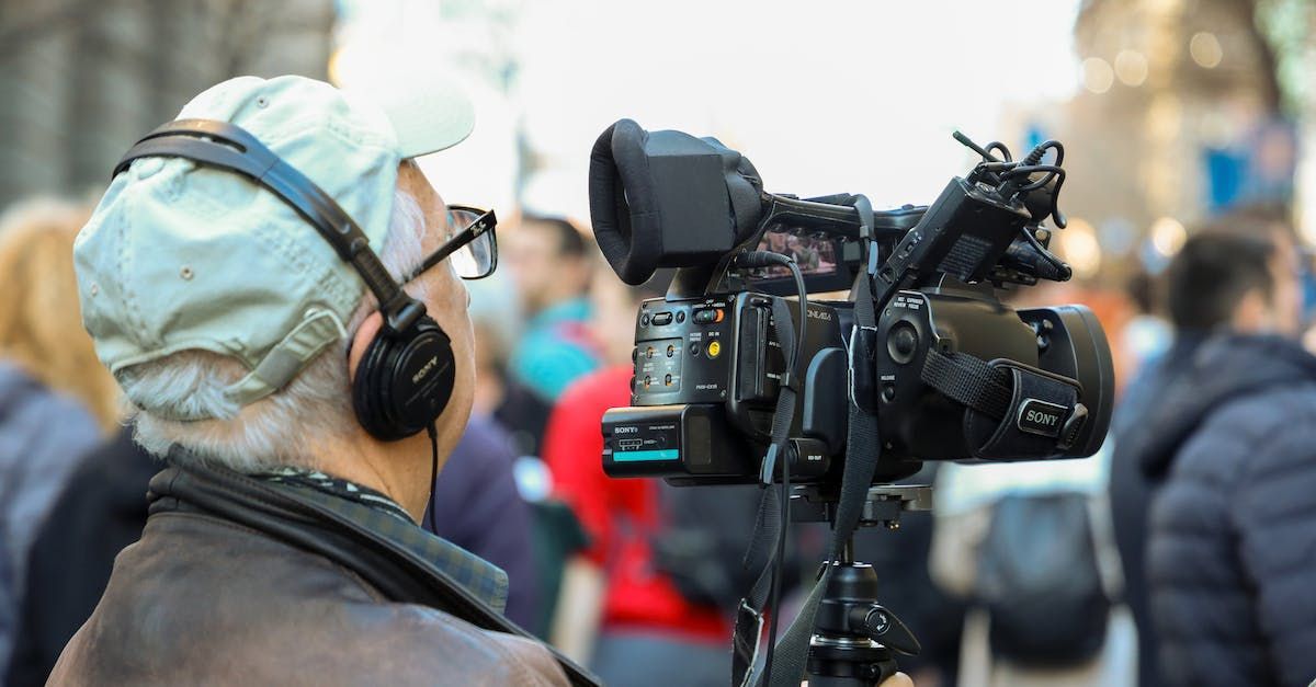 A man wearing headphones is holding a camera in front of a crowd of people.