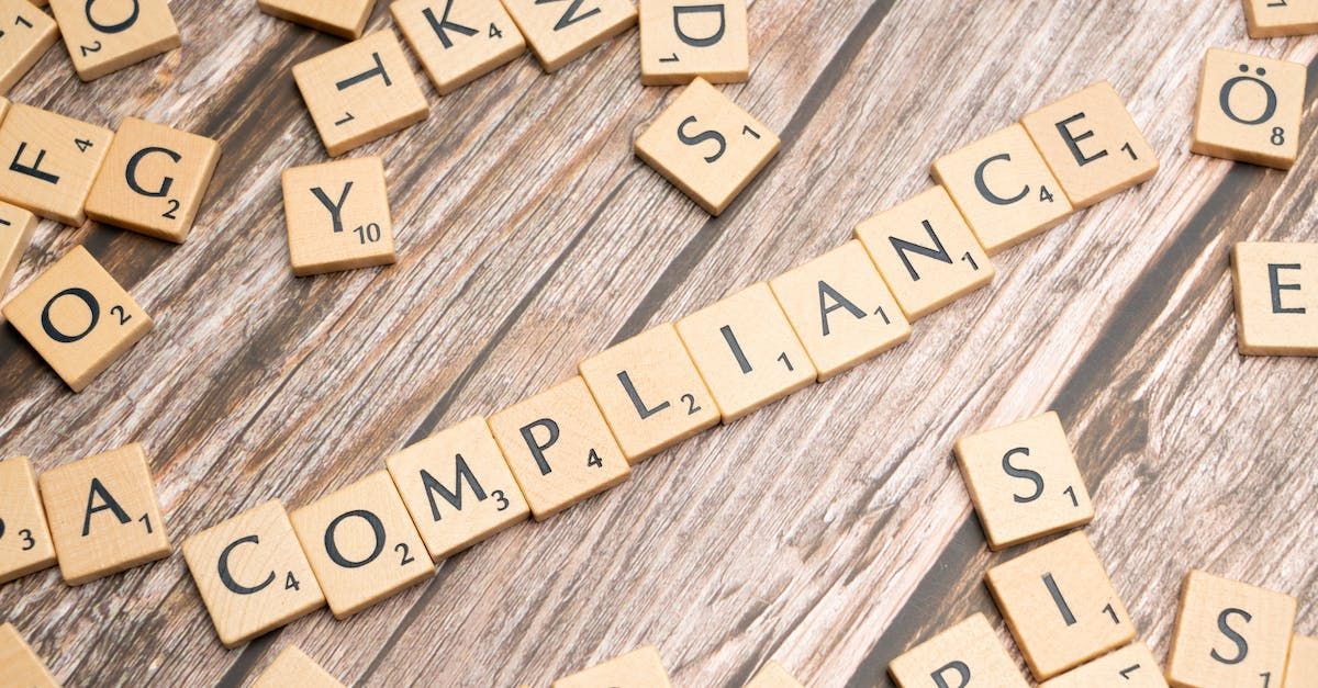 The word compliance is written in scrabble tiles on a wooden table.