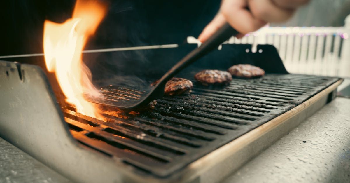 Hand flipping burgers on a flaming outdoor grill with hot coals and smoke