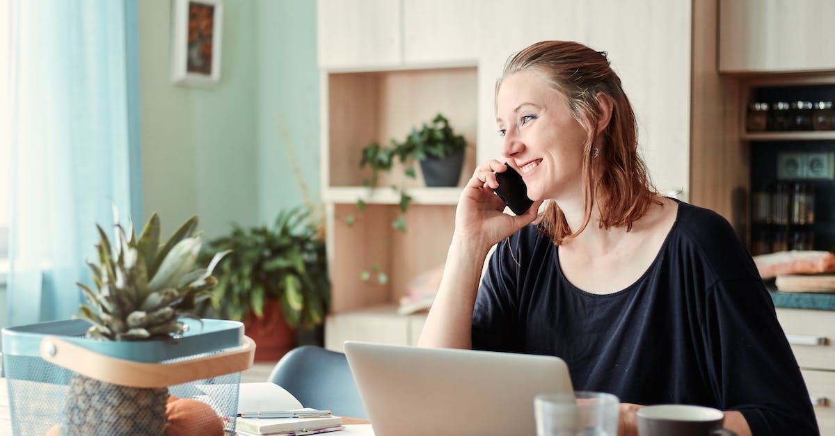 A woman is sitting at a table with a laptop and talking on a cell phone.
