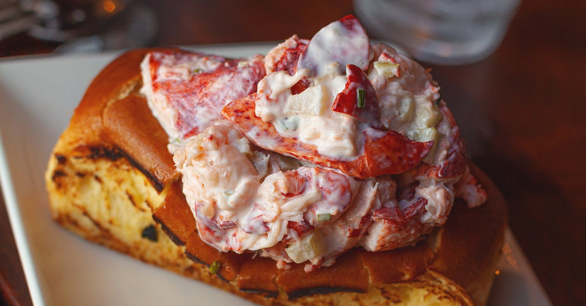 A close up of a lobster roll on a white plate on a table.