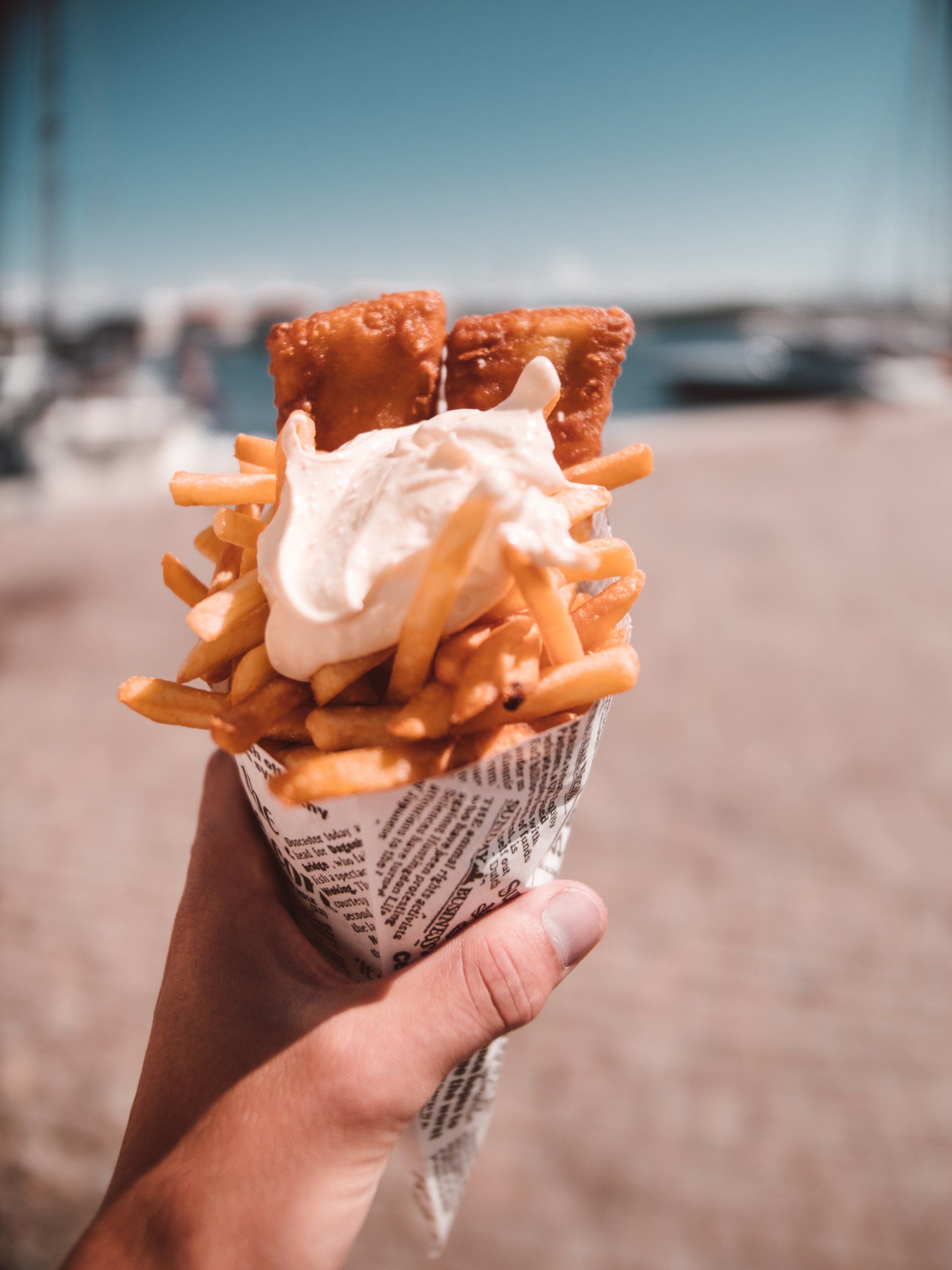 A person is holding a cone of fish and french fries.