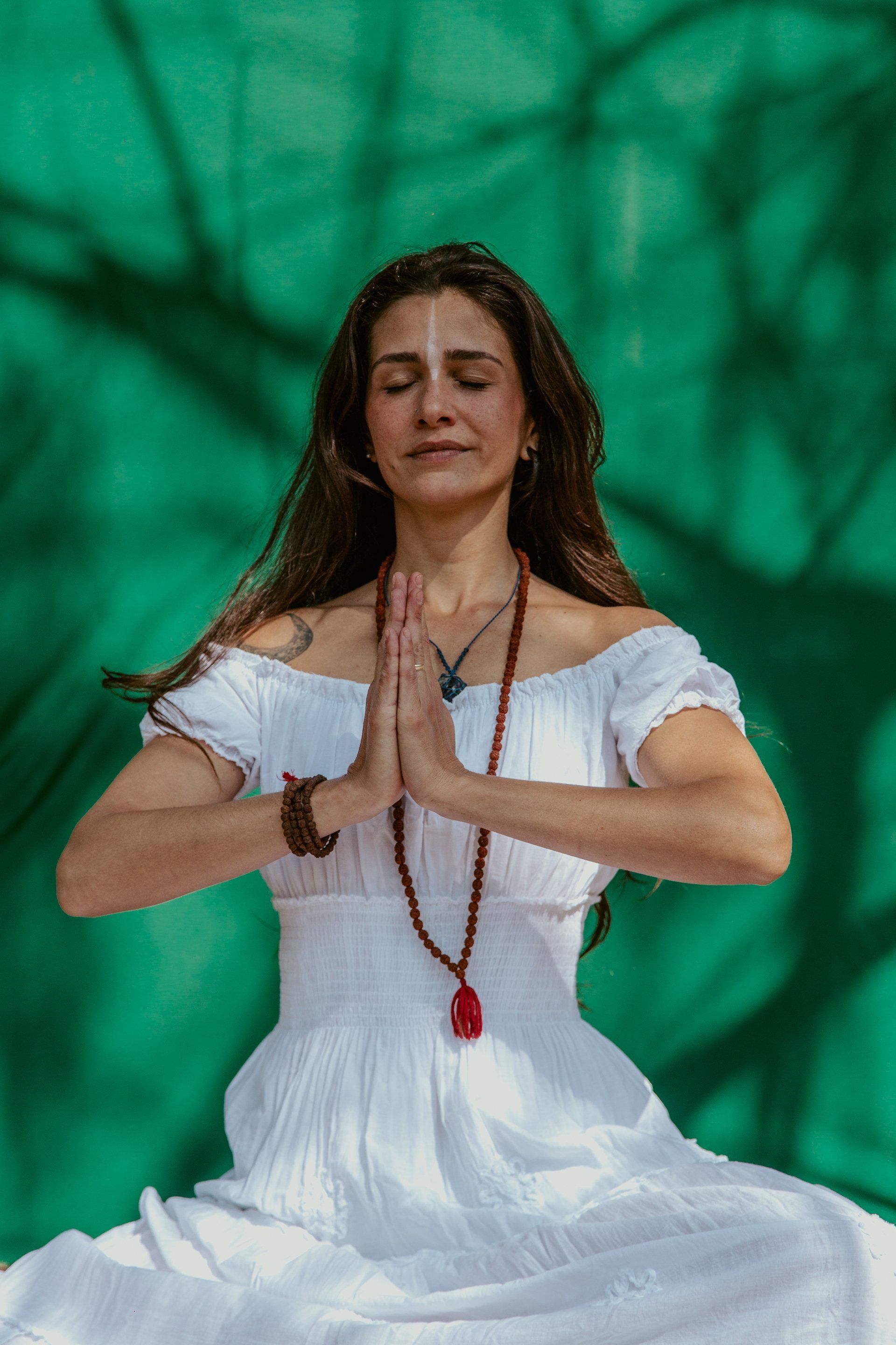 A woman in a white dress is sitting in a lotus position with her eyes closed.