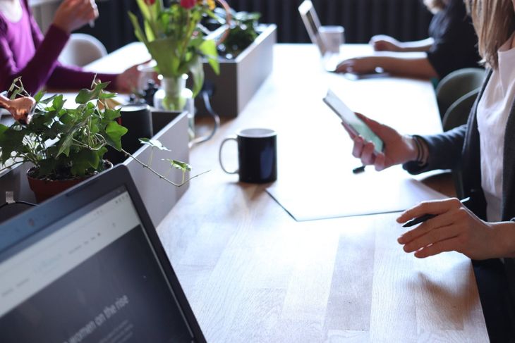 A group of people are sitting at a table using laptops and cell phones.