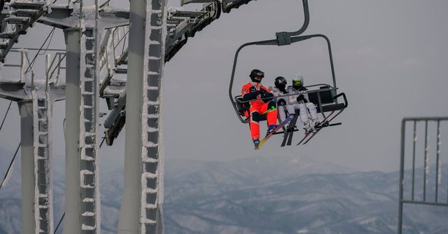 Télésiège transportant deux personnes vêtues de vêtements aux couleurs vives au-dessus d'un paysage de montagne enneigé