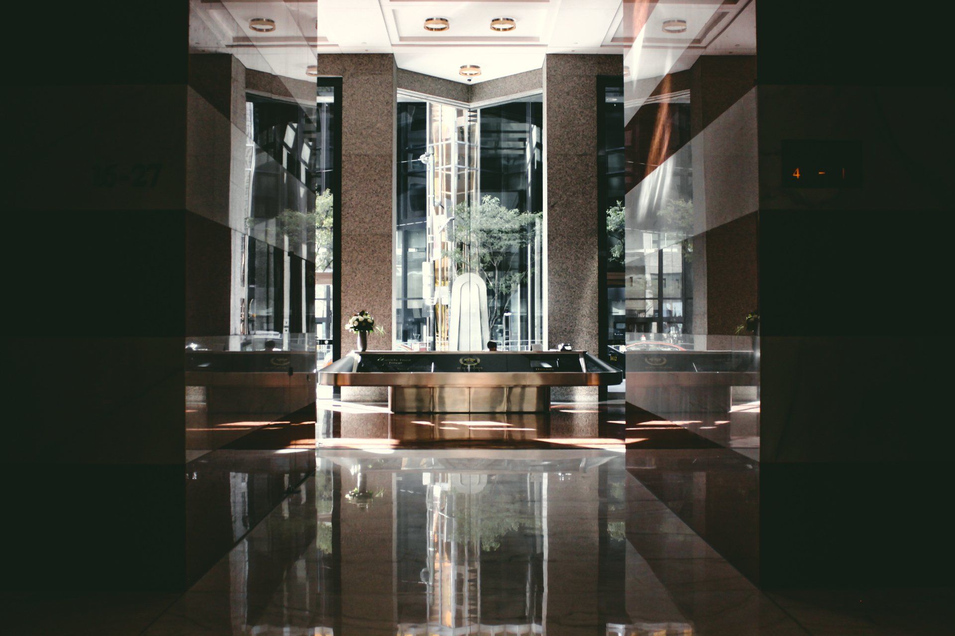 Interior view of a modern building with large windows, reflecting light onto a shiny floor. A statue is visible in the center.