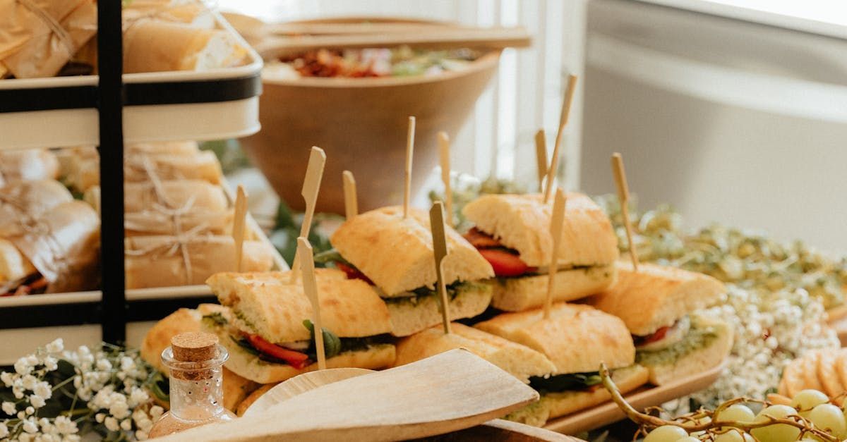 Sandwich appetizers on a wooden platter, with toothpicks. Food display, surrounded by greenery and wooden serving utensils.