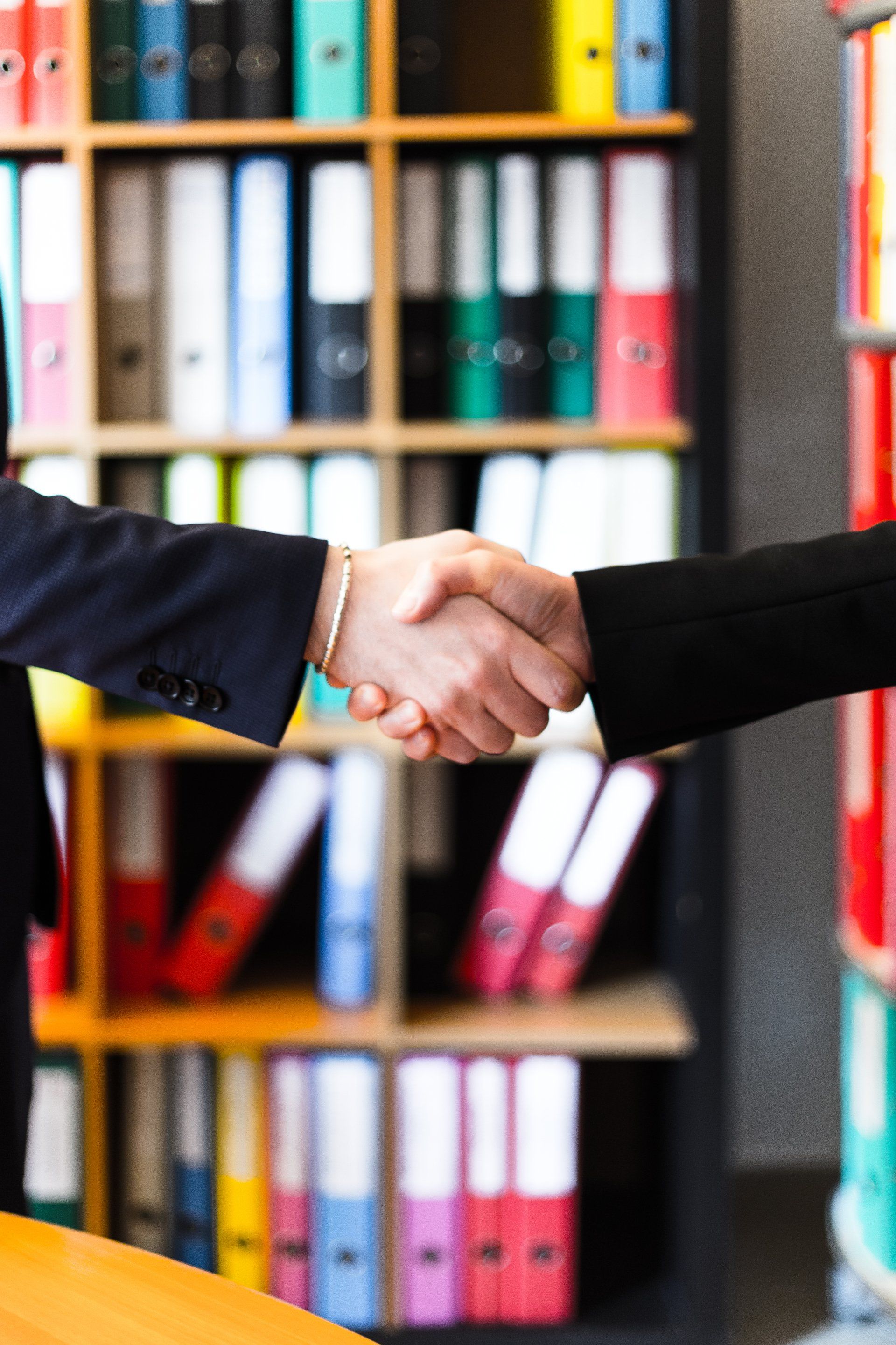 Two people shaking hands in front of a bookshelf full of binders.
