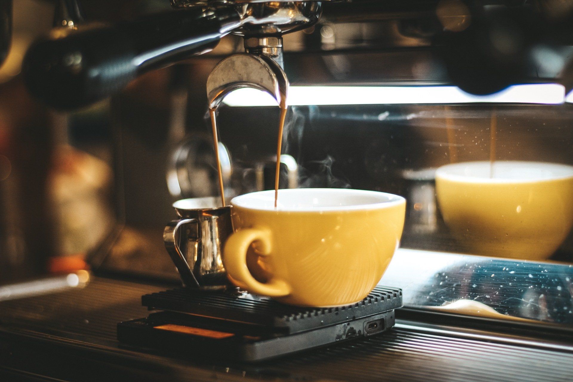 A yellow cup of coffee is being poured into a coffee machine.
