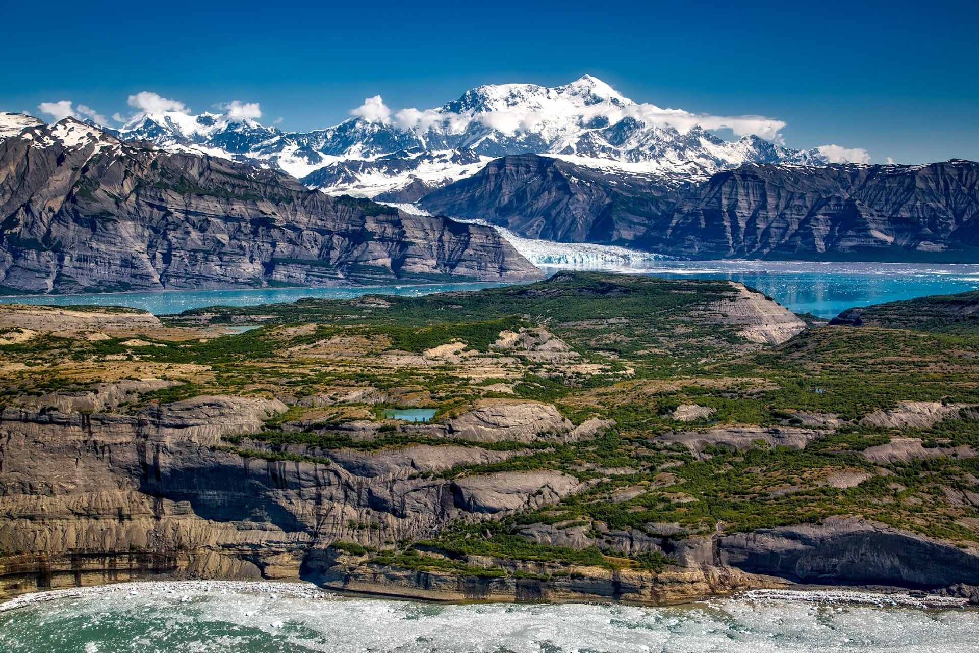 A landscape with mountains and a lake in the foreground and a glacier in the background.