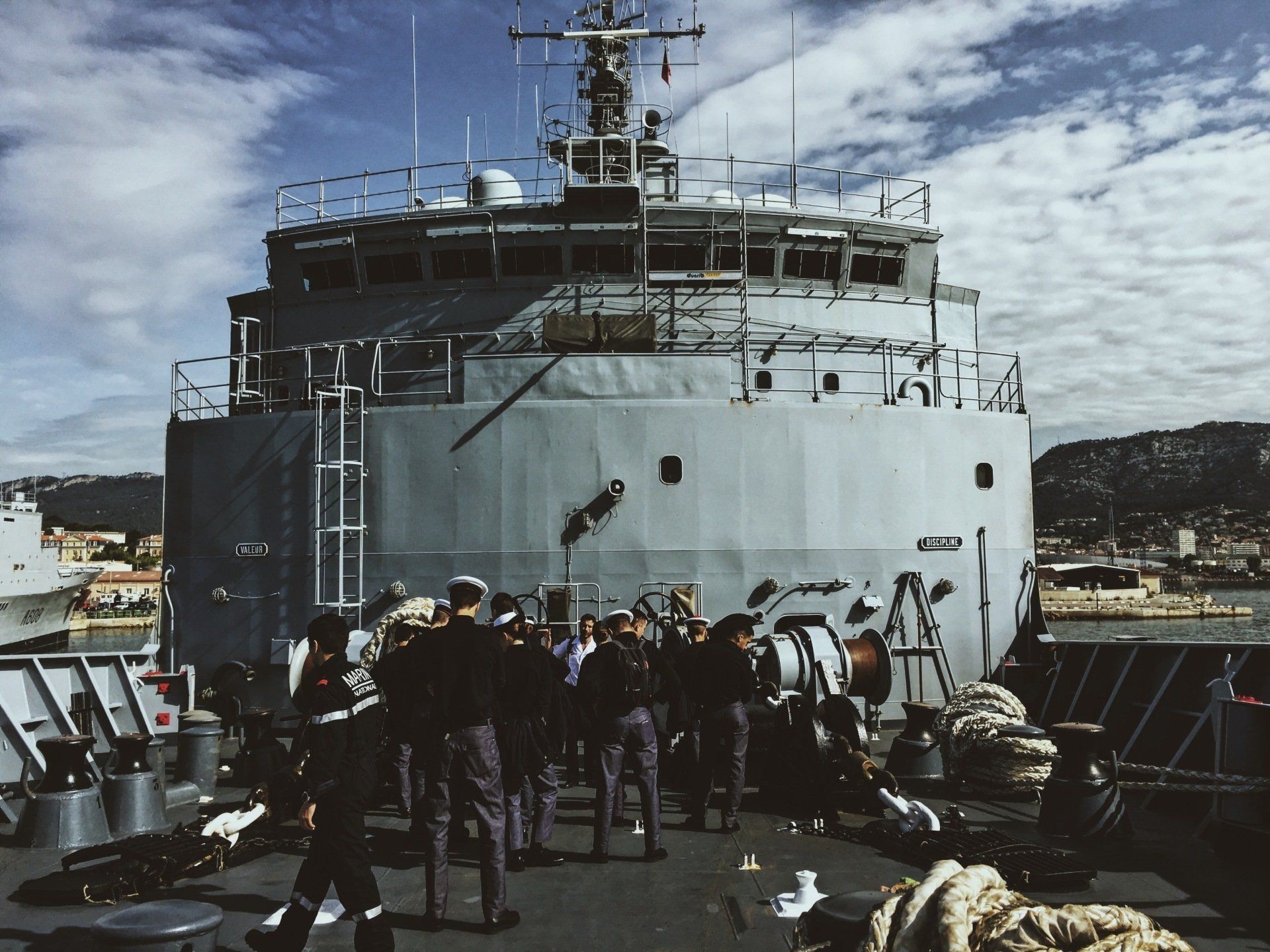Navy personnel on deck of grey ship in port, under blue sky.