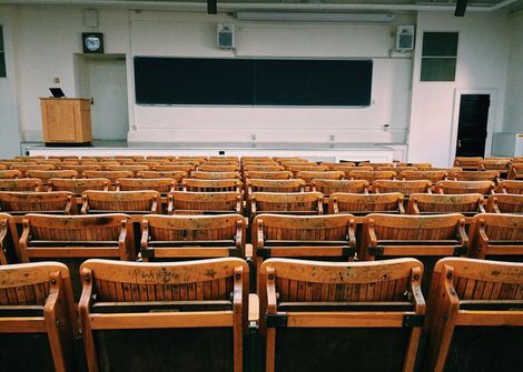 Rows of wooden chairs in an auditorium with a blackboard in the background