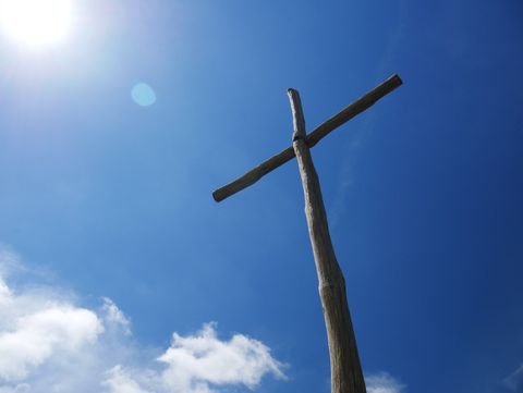 A wooden cross against a blue sky with clouds