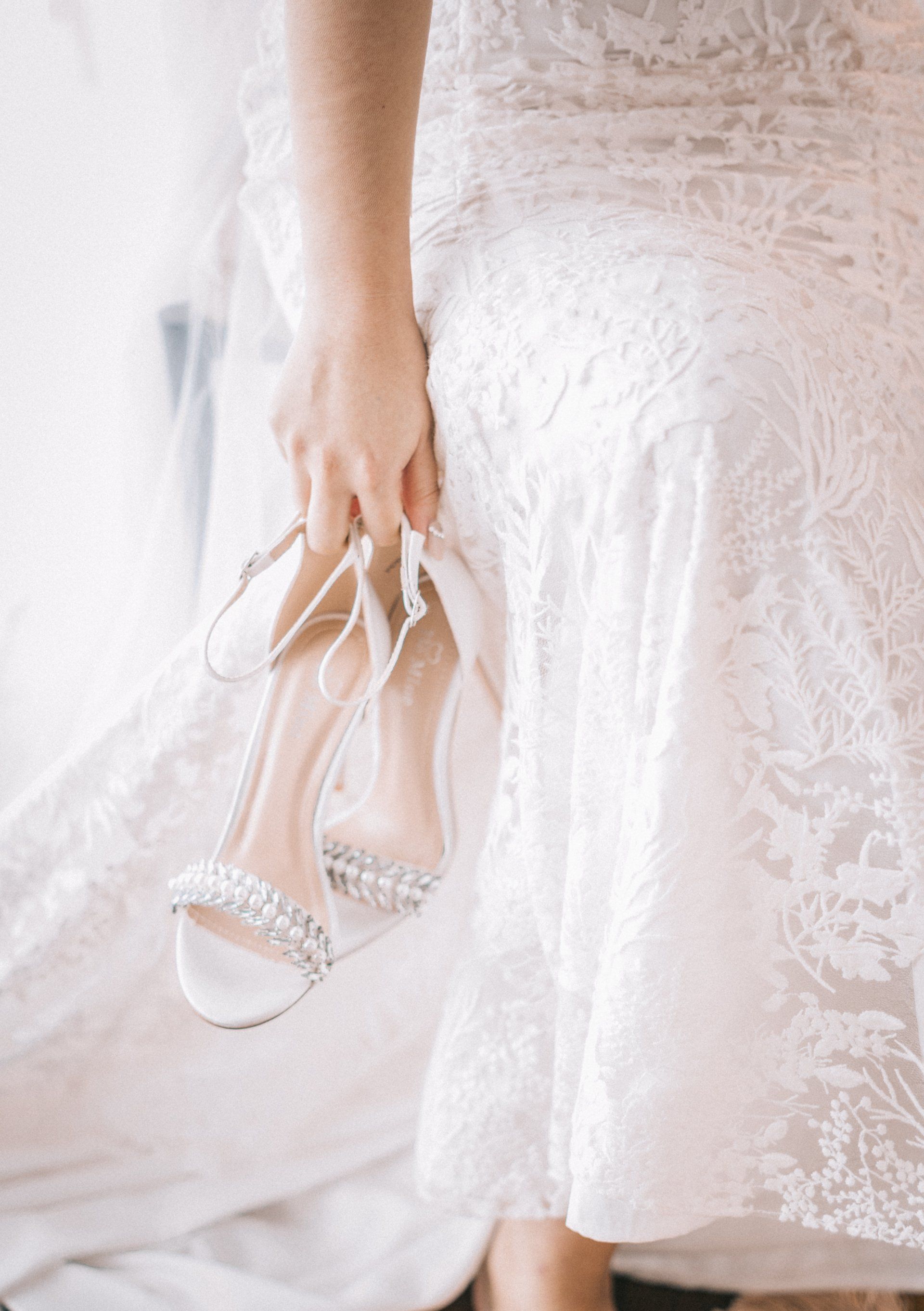 A woman in a white dress is holding a pair of wedding shoes.