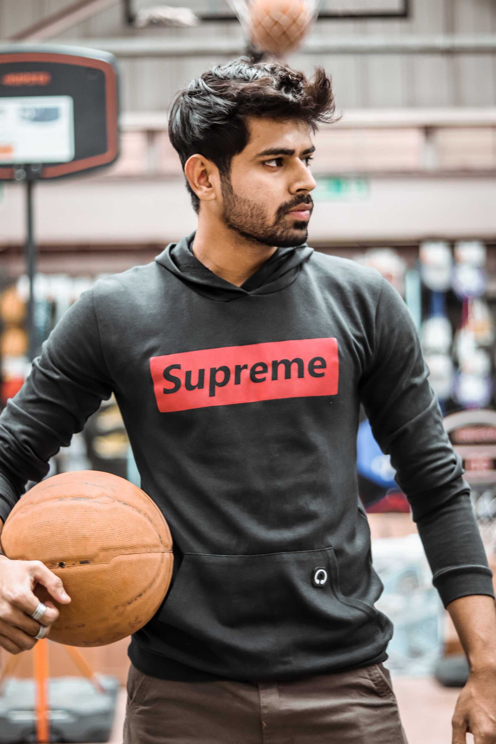 Um homem vestindo um moletom supreme está segurando uma bola de basquete.