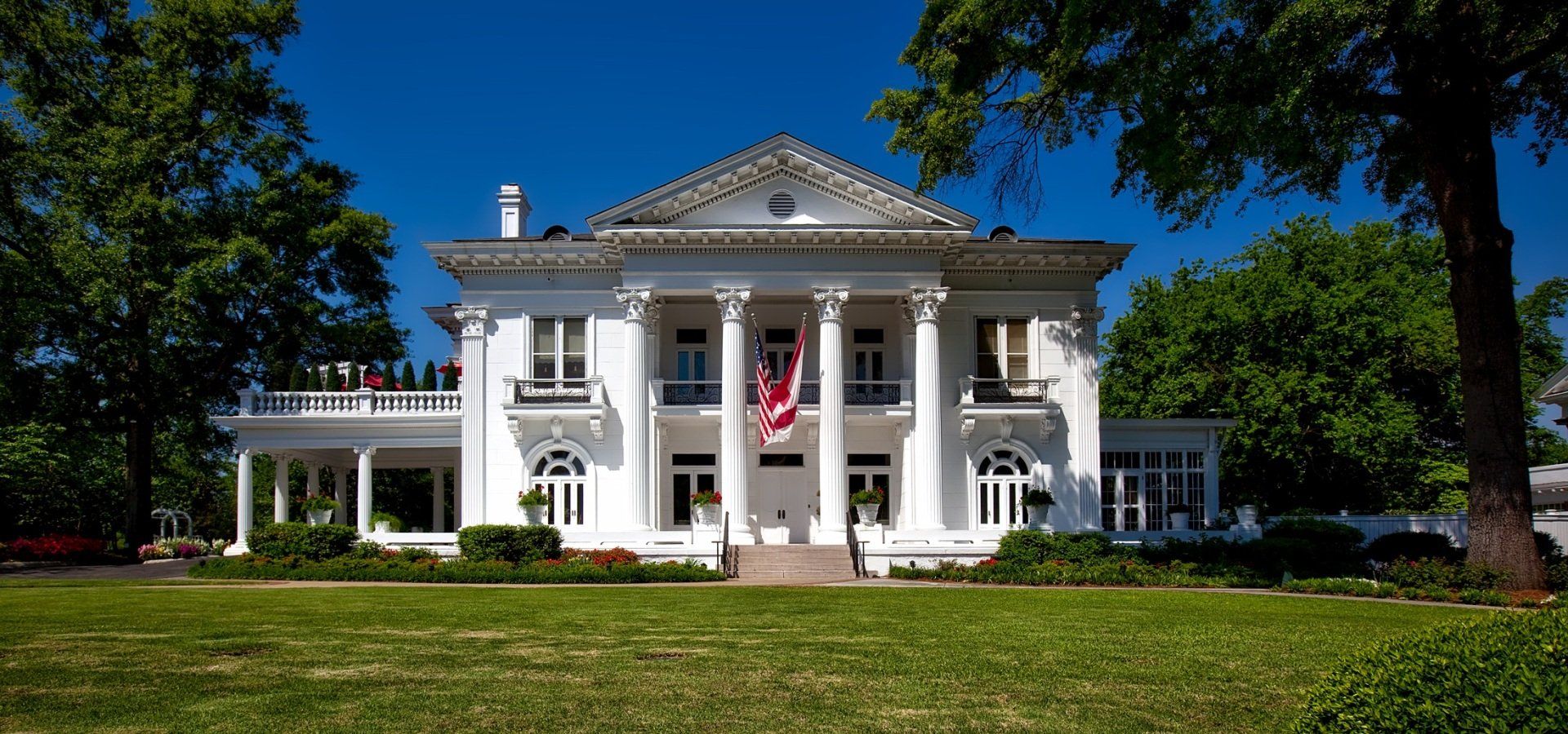 A large white house with a red flag flying in front of it.