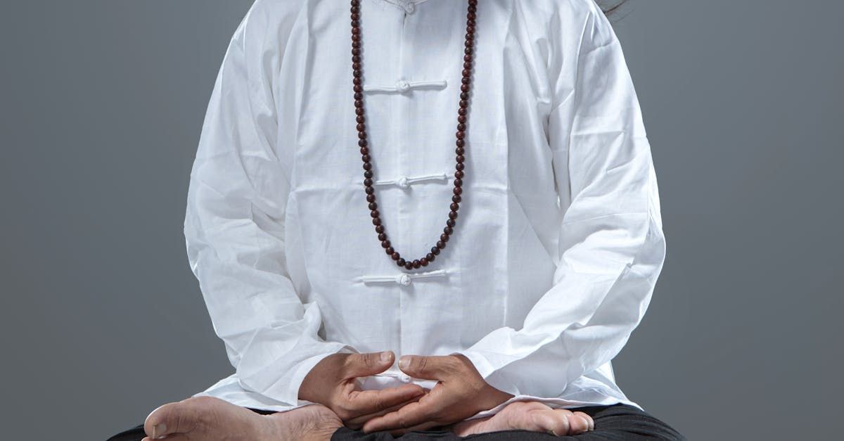 Person in white shirt and prayer beads meditating in a lotus position.