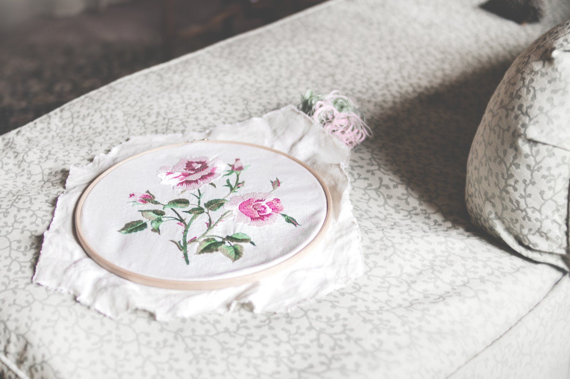 A cross stitch embroidery hoop is sitting on a couch.