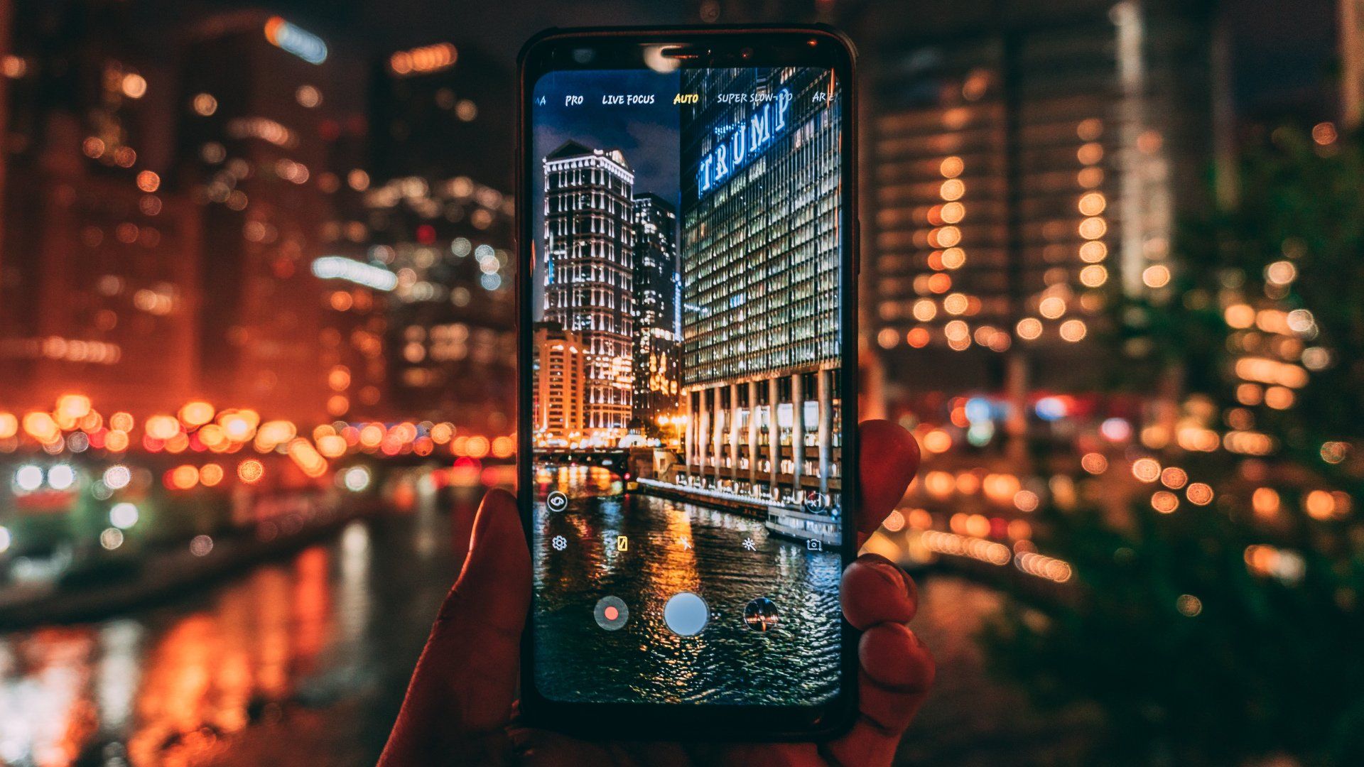 Hand holding a smartphone showing a city street at night with bright lights and reflections