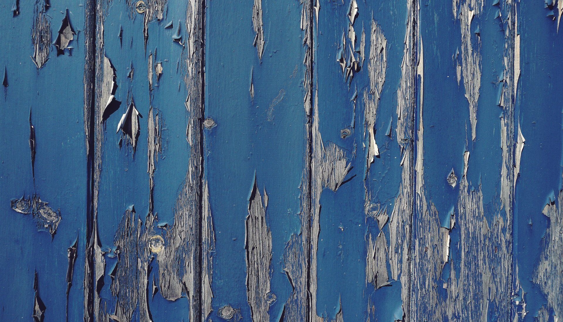 Weathered blue wooden surface with peeling white paint and vertical cracks