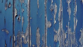 Weathered blue wooden surface with peeling white paint and vertical cracks
