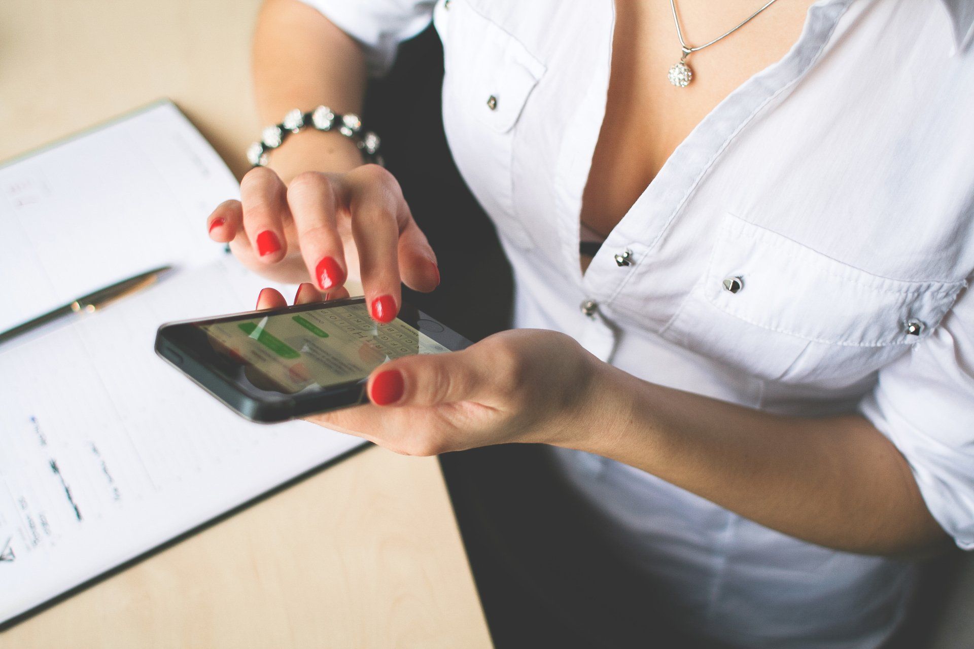 A woman with red nails is using a cell phone.
