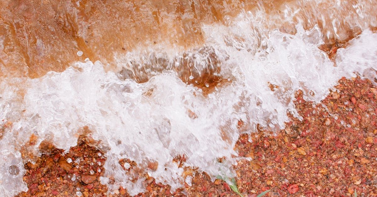 White foamy water washes over a reddish-brown, pebbly beach.