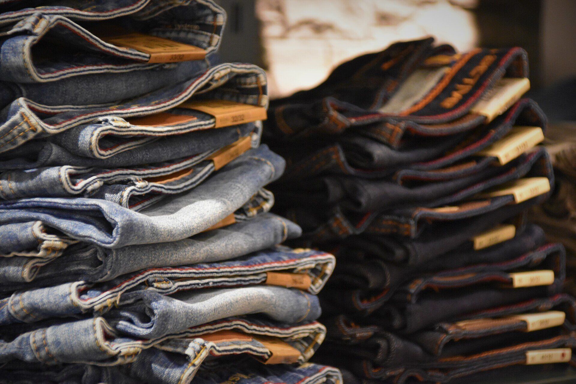 Stacks of folded blue and dark denim jeans, displayed on a shelf.