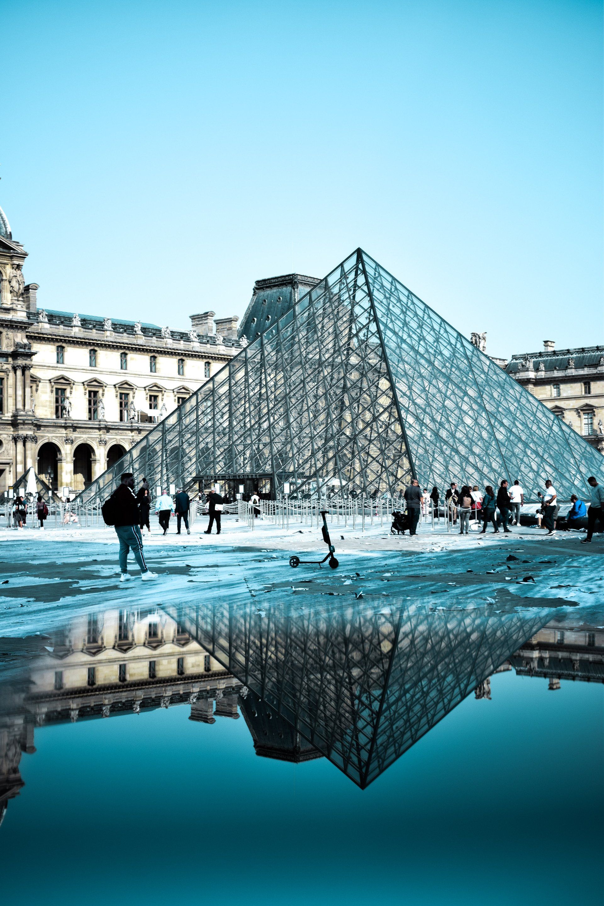 A large glass pyramid is reflected in a puddle of water.