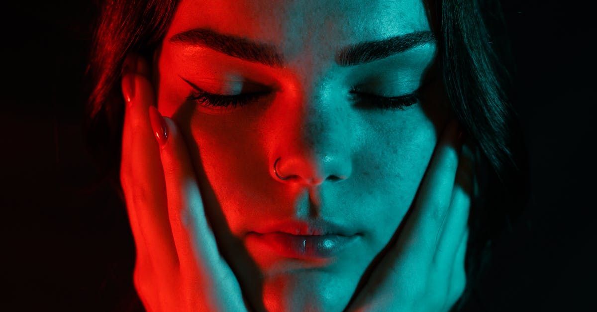 A teenager is covering her face with her hands in red and blue light.