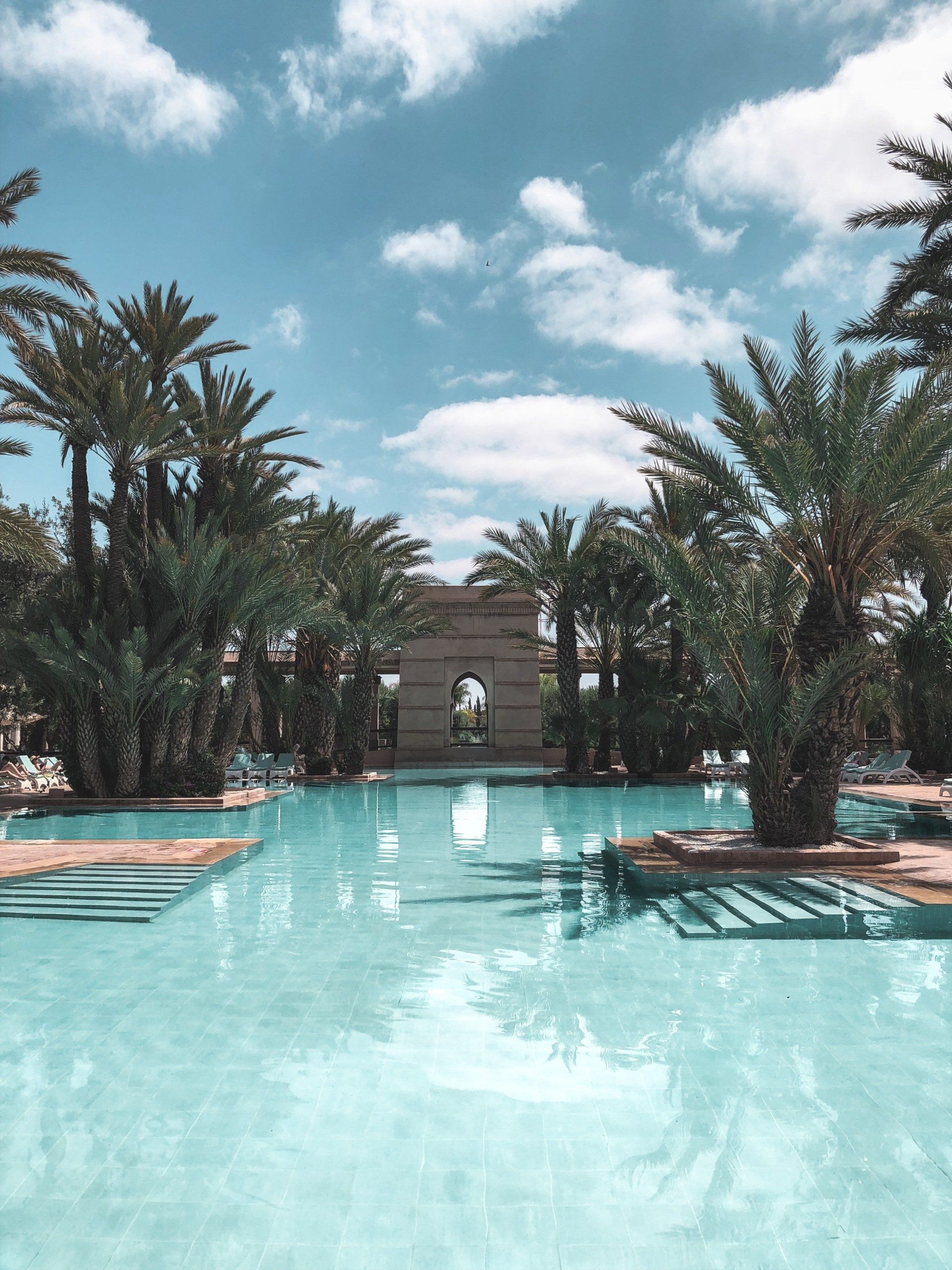Turquoise pool framed by palm trees and lounge chairs under a cloudy sky